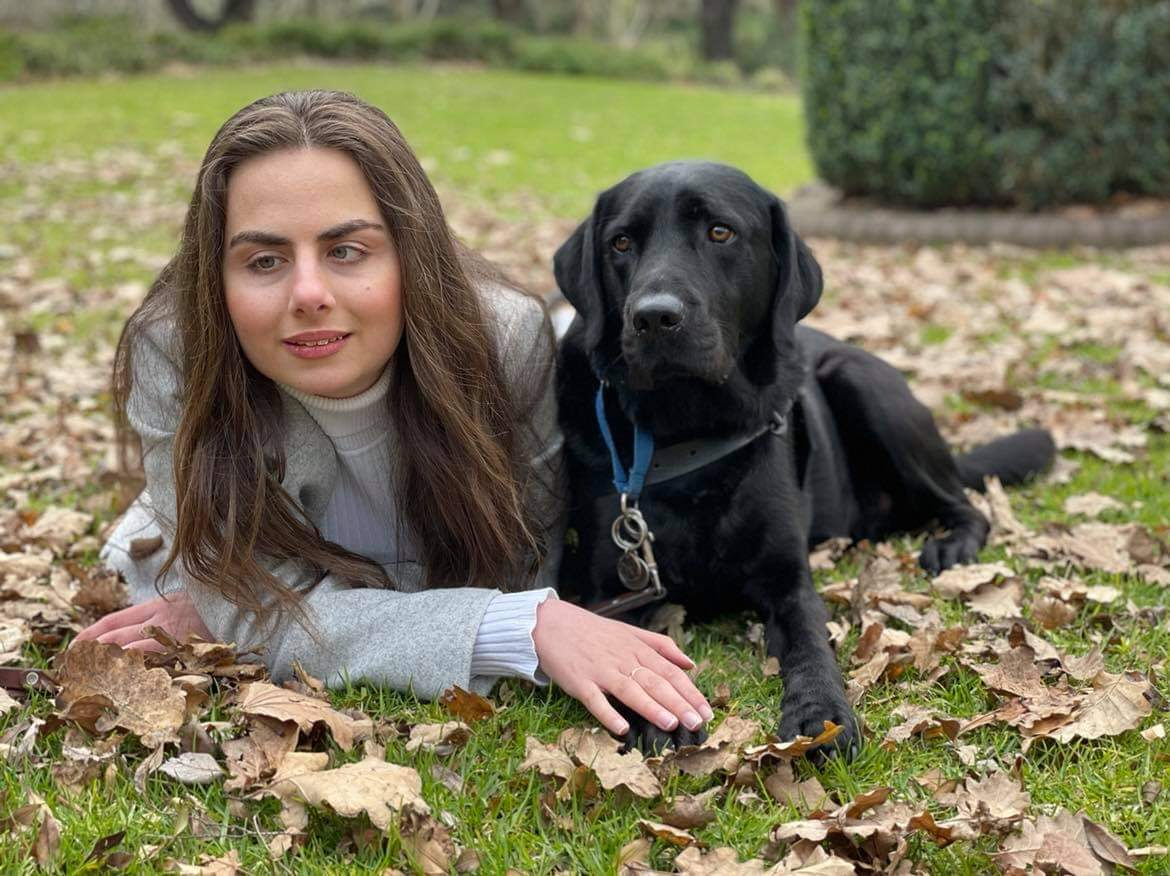 A woman with a visual impairment and her guide dog laying on the grass.